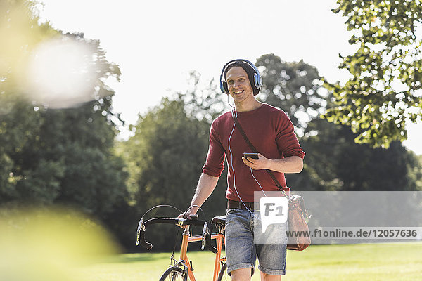 Smiling man with racing cycle listening music with headphones in a park