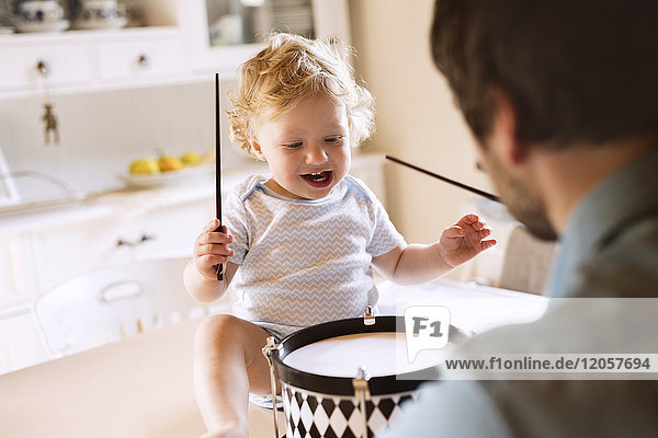 Father with happy little boy sitting on kitchen table playing drum