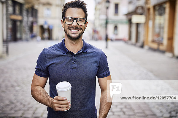 Portrait of a smiling man with glasses holding coffee outdoors