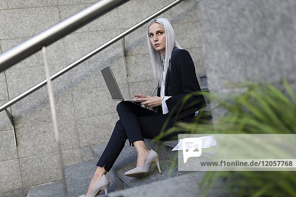 Junge Geschäftsfrau sitzend auf einer Treppe in der Stadt mit Laptop