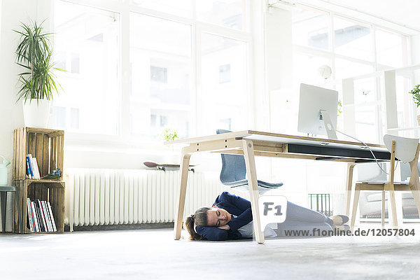 Businesswoman lying under the table in office sleeping