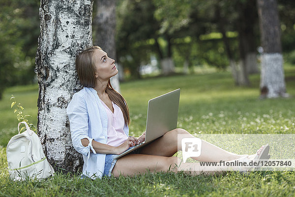 Young woman with laptop on a meadow looking up