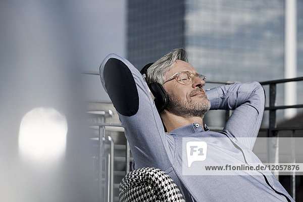 Grauhaariger Mann,  der sich auf dem Balkon entspannt und Musik hört