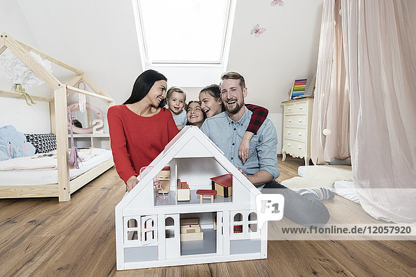 Glückliche Familie mit drei Töchtern  die hinter dem Puppenhaus im Kinderzimmer sitzen.