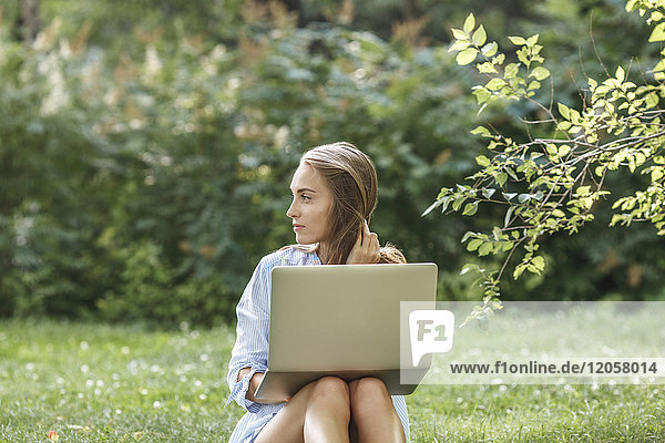 Junge Frau mit Laptop auf einer Wiese mit Blick zur Seite