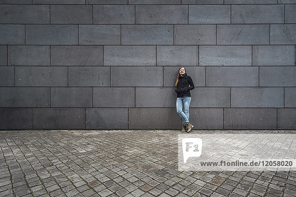 Young woman standing in front of grey facade waiting