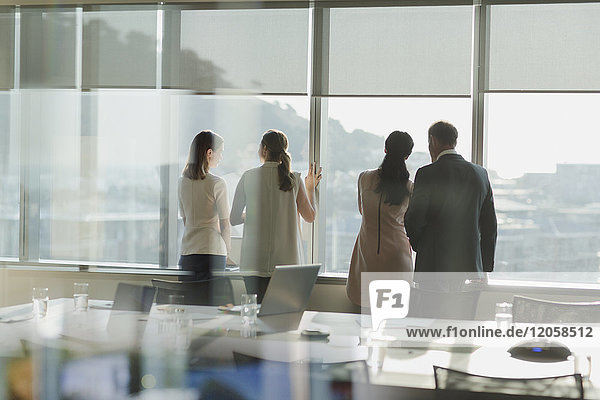 Geschäftsleute schauen aus einem sonnigen Fenster in einem städtischen Konferenzraum