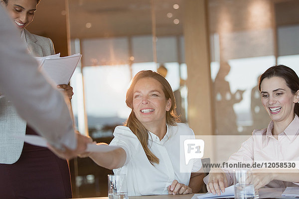 Lächelnde Geschäftsfrau  die einem Kollegen in einem Konferenzraum Papierkram übergibt