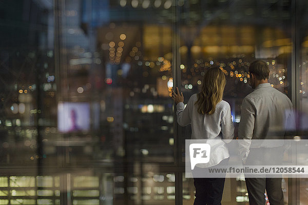 Geschäftsmann und Geschäftsfrau schauen nachts aus dem Fenster eines städtischen Büros