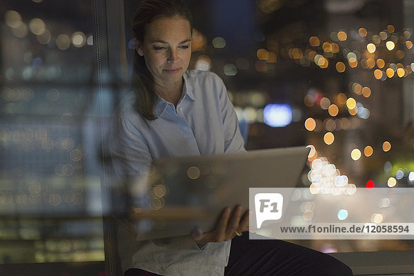 Seriöse Geschäftsfrau  die nachts am Laptop im Bürofenster arbeitet