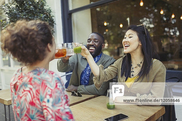 Smiling enthusiastic friends toasting fresh juice glasses at sidewalk cafe
