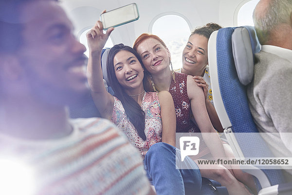 Junge Freundinnen mit Fotohandy  die Selfie im Flugzeug mitnehmen.