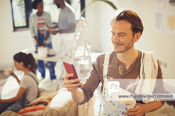 Mann malt Wohnzimmer  trinkt Kaffee und überprüft Smartphone