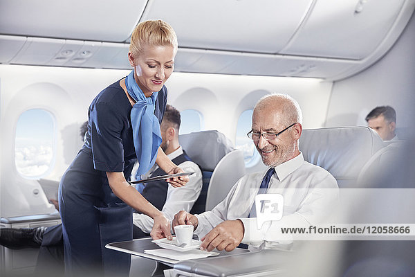 Flugbegleiterin mit Espresso-Kaffee für Geschäftsleute in der ersten Klasse im Flugzeug