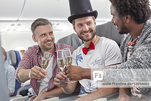 Junge männliche Freunde stoßen im Flugzeug auf Champagnergläser an.