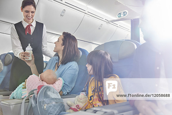 Lächelnde Flugbegleiterin bringt Babyflasche zur Mutter mit Baby im Flugzeug