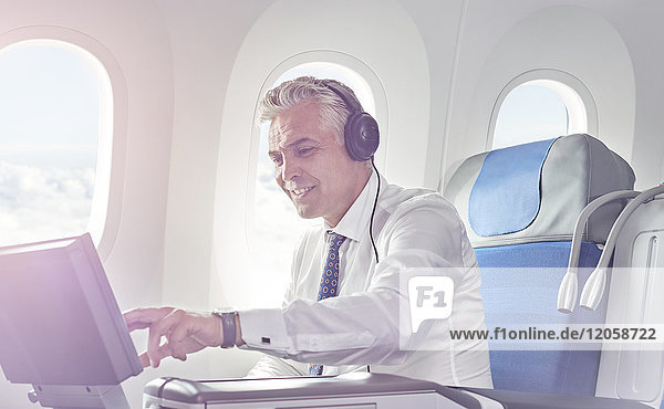Geschäftsmann mit Kopfhörer,  der sich einen Film im Flugzeug ansieht