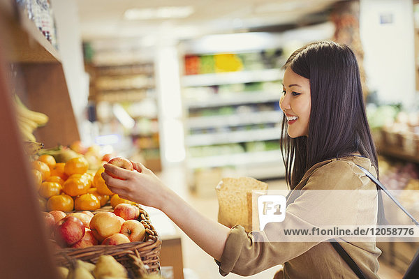 Smiling young woman shopping for apples in grocery store