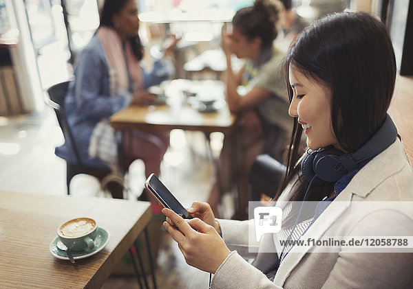 Lächelnde junge Frau beim SMSen mit Handy und Kaffeetrinken am Cafe Tisch