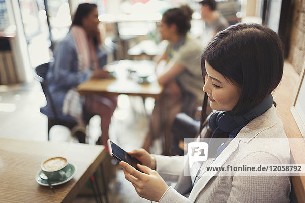 Junge Frau mit Kopfhörer SMS mit Handy und Kaffeetrinken am Cafe Tisch