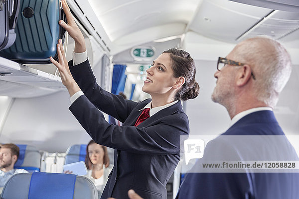 Flugbegleiterin hilft Geschäftsmann  Gepäck in den Gepäckraum des Flugzeugs zu legen