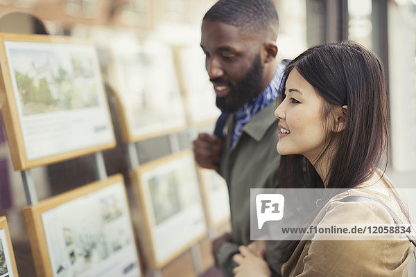 Smiling young couple looking at real estate listings at storefront