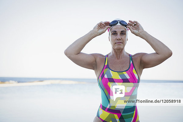 Portrait serious  tough mature female open water swimmer adjusting swimming goggles at ocean