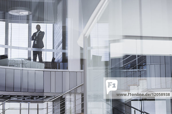 Zuversichtlicher CEO Geschäftsmann steht mit gekreuzten Armen am modernen Bürofenster