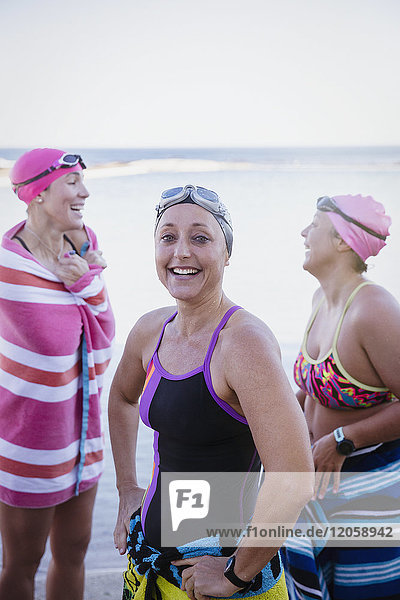 Portrait lächelnde  selbstbewusste Schwimmerinnen  die mit Handtüchern am Meer trocknen.