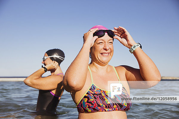 Smiling  happy female open water swimmer adjusting swimming goggles in sunny ocean