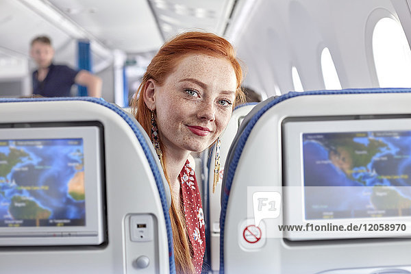 Portrait lächelnde junge Frau mit roten Haaren und Sommersprossen im Flugzeug