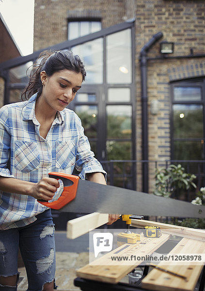 Young woman with saw cutting wood on patio