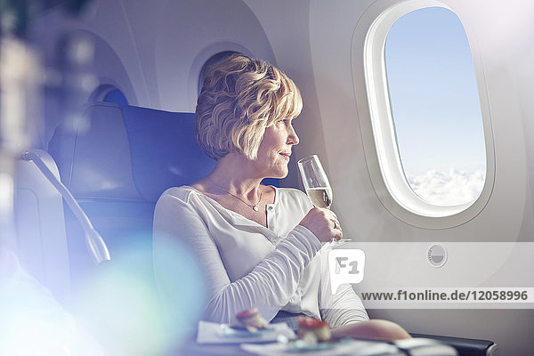 Reife Frau trinkt Champagner  schaut aus dem Fenster in der ersten Klasse im Flugzeug.