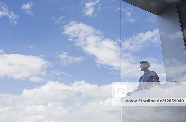 Nachdenklicher Geschäftsmann auf dem modernen Balkon mit Blick auf sonnigen blauen Himmel und Wolken.
