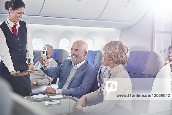 Flugbegleiterin serviert Champagner für ein reifes Paar in der ersten Klasse im Flugzeug.