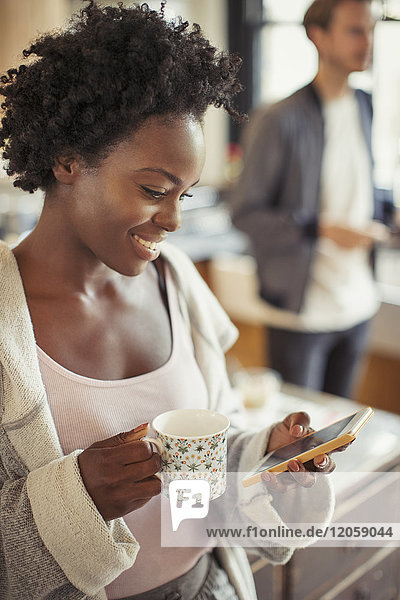 Lächelnde Frau trinkt Kaffee  SMS mit Smartphone