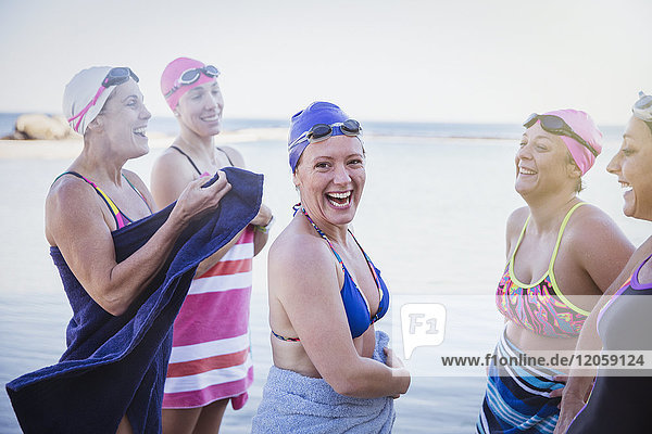 Portrait lächelnde Schwimmerinnen  die mit Handtüchern im Meer abtrocknen