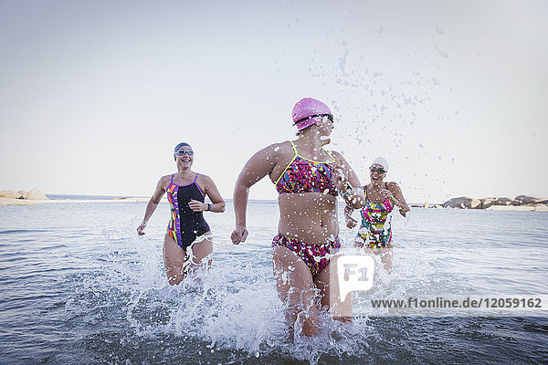 Weibliche Freischwimmerinnen beim Laufen  Planschen in der Brandung