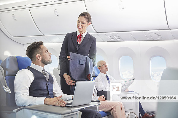 Flugbegleiterin im Gespräch mit Geschäftsmann am Laptop im Flugzeug