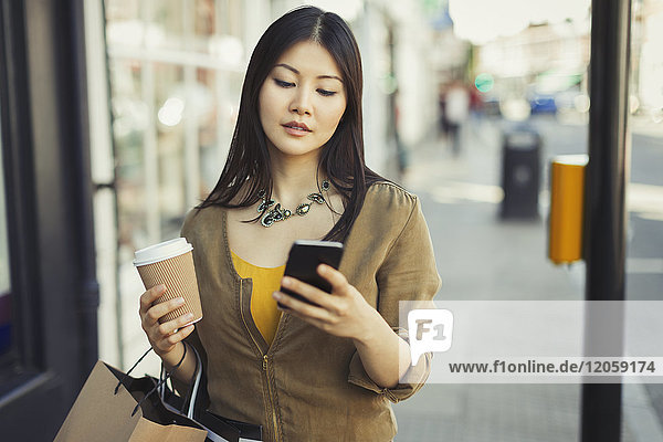 Young woman with coffee texting with cell phone on urban sidewalk