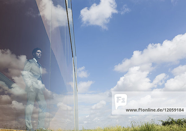 Nachdenklicher Geschäftsmann mit Blick aus dem modernen Bürofenster auf sonnigen blauen Himmel und Wolken