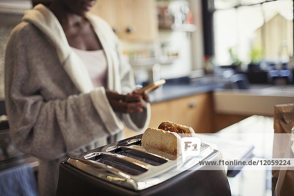 Frau SMS mit Smartphone  Toastbrot im Toaster in der Küche