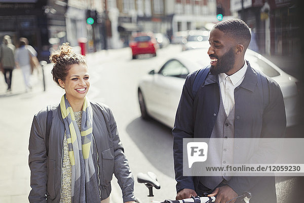 Lächelndes Paar  das mit dem Fahrrad auf einer sonnigen Stadtstraße pendelt.