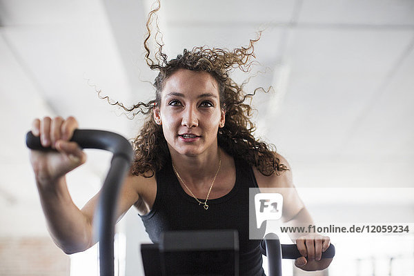 Determined young woman using elliptical trainer in gym