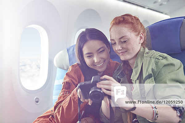 Lächelnde junge Freundinnen beim Betrachten von Fotos auf der Digitalkamera im Flugzeug
