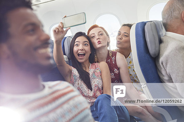 Verspielte junge Freunde mit Fotohandy  die Selfie im Flugzeug mitnehmen.