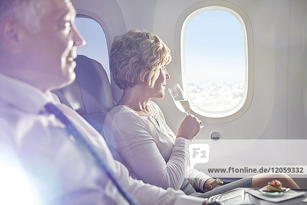Frau trinkt Champagner in der ersten Klasse  blickt aus dem Flugzeugfenster