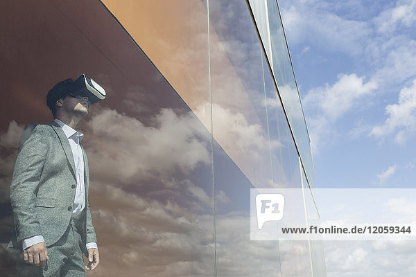 Geschäftsmann mit Virtual-Reality-Simulator-Brille am modernen Fenster mit Wolkenreflexion