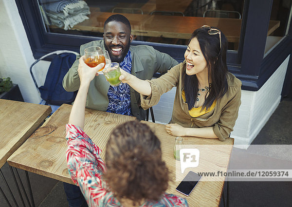Enthusiastic friends toasting fresh juice glasses at sidewalk cafe