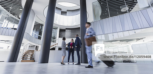 Business people talking and pulling suitcase in architectural  modern office lobby